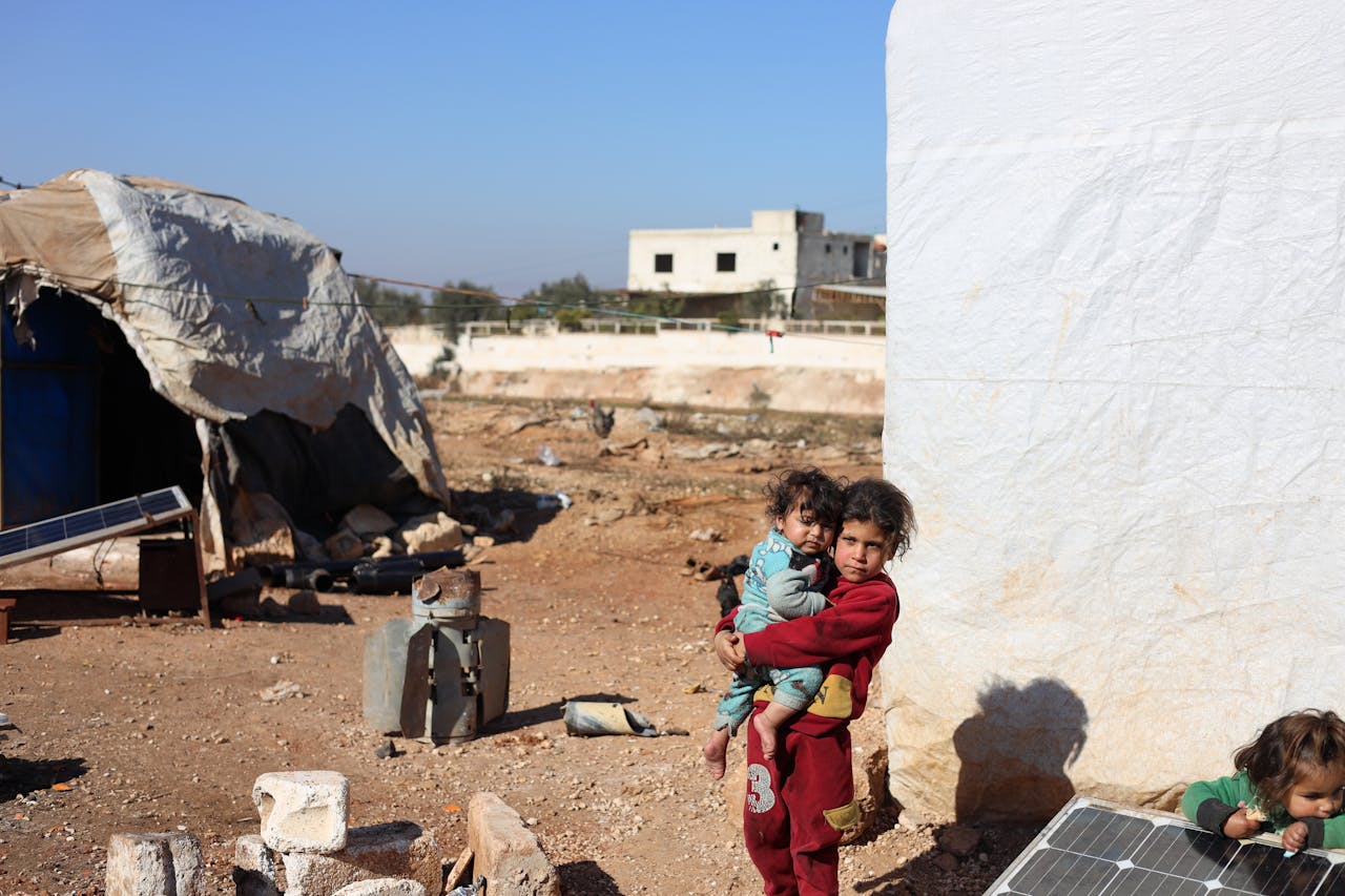 Two children stand outside shelter in Idlib refugee camp, Syria.